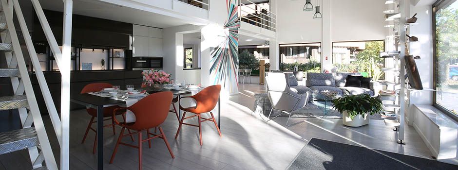 Lo showroom Minola: tavolo con sedie arancioni, divano e la scala verso il soppalco